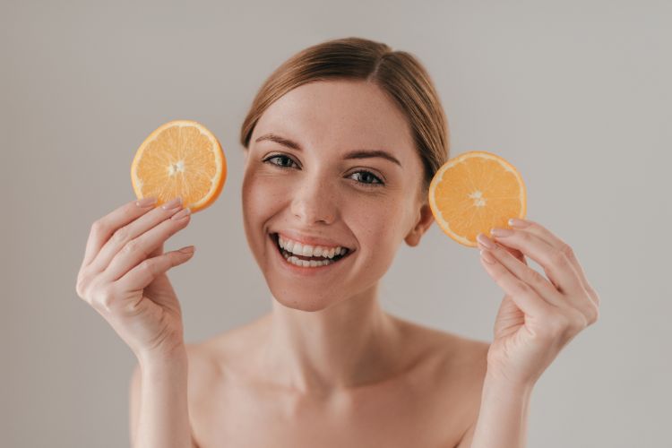 Devojka se osmehuje i drži u rukama dva koluta pomorandže.